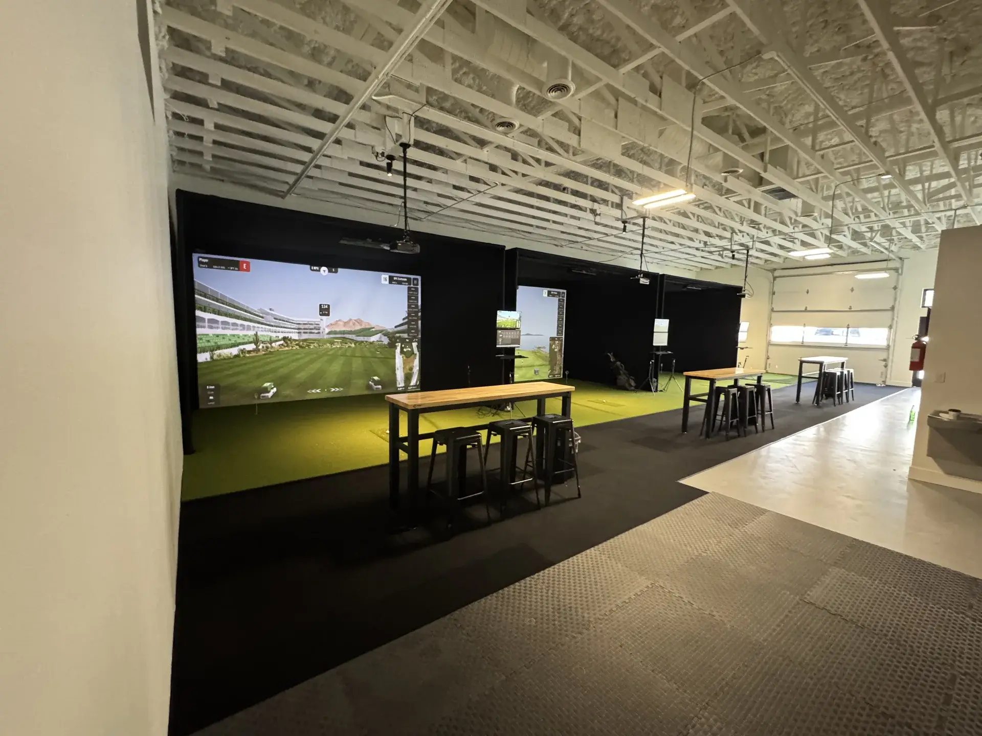Three golf simulator bays with high-top tables at Summit Golf Lab in Elizabeth, CO